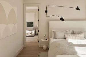 A modern minimalist bedroom with a simple white bed, white linens, and a soft fabric headboard.