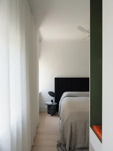 A minimalist bedroom featuring neutral fabrics and a large window with sheer curtains.
