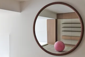 A minimalist interior space featuring a wooden lattice screen, a large grey ball centered on a rug, and a large window.