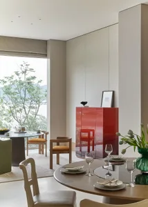 A modern minimalist dining room with a circular table, chairs, and a red cabinet.