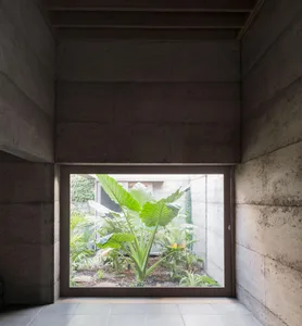 A modern interior space with concrete walls and a view of a lush green garden. 