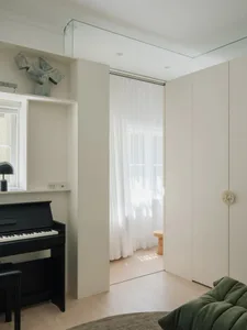 A minimalist bedroom with neutral-colored walls and furniture, featuring a black piano and green cushions.