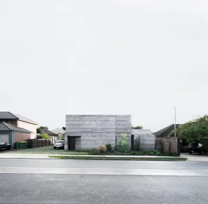 A modern concrete residential house with a minimalist aesthetic, featuring a single-story structure with a flat roof and mini