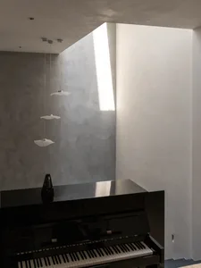 Modern minimalist music room with concrete walls, a piano, and pendant lights.