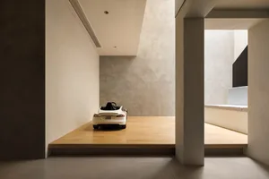 Modern minimalist interior with concrete walls and floors, featuring a sleek white car on a raised platform.