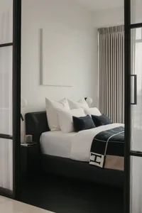 Minimalist bedroom featuring a bed adorned with black and white textiles, positioned near tall, closed drapes.