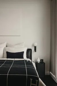 A minimalist bedroom featuring a black and white checkered blanket, a white pillow, and a leather bedframe.