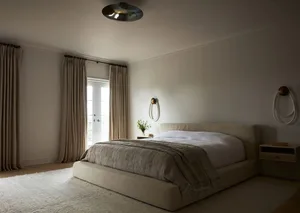 A minimalist bedroom with grey textiles and a neutral color palette, featuring a large bed with a beige headboard, a modern l