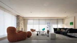 Modern minimalist lounge area featuring a concrete floor and walls, with a black sofa, a colorful striped armchair, and a gla
