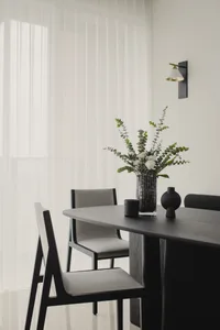 A modern dining room with wooden furniture, including chairs and a table, adorned with a vase of flowers and decorative objec