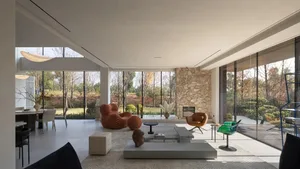 Modern living room with glass walls, featuring minimalist furniture and a stone fireplace.