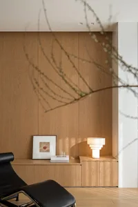 A modern minimalist living room with wooden paneling, featuring a sleek black lounge chair, a framed artwork, and a contempor