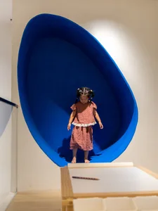 A child stands inside a blue, egg-shaped space in a playroom.