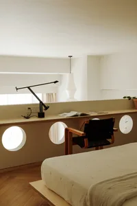 A minimalist bedroom featuring a simple bed with a wooden frame, a black leather armchair, and a floating desk with a black l