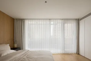 A minimalist bedroom with a large window covered by sheer white curtains.