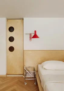 A minimalist bedroom featuring a wooden headboard panel and a red sconce light.