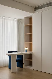 A minimalist home office featuring a white desk, blue chair, and white oak shelves.