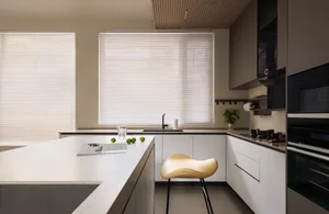 A minimalist kitchen with neutral tones, featuring a white countertop, modern appliances, and a single stool.
