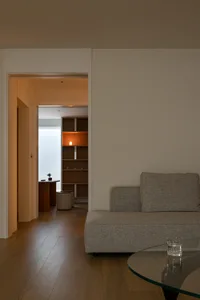 Minimalist living room with a gray couch, wooden floor, and soft lighting.