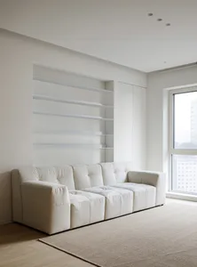 A minimalist white living room featuring a textured couch, plush blankets, and shelves.