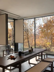 A modern coffee shop featuring a wooden counter with a tea set and autumn leaves outside the large windows.