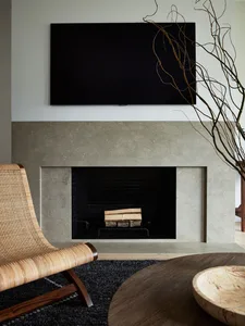 A modern living room with concrete fireplace, woven chair, wooden table, and minimalist decor.
