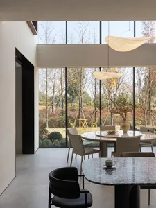 A modern dining room featuring concrete flooring and walls with large windows overlooking a garden.