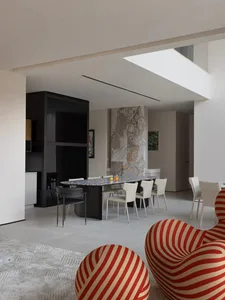 Modern dining room featuring a long, oval marble table surrounded by white chairs, set against a marble feature wall.