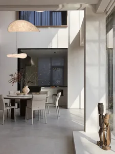 Modern dining room with a round table, white chairs, and a vase of dried flowers on the table, with a kitchen area in the bac