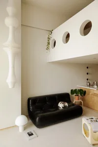 A modern living room with a black leather sofa, a white floor lamp, and a beige carpet.