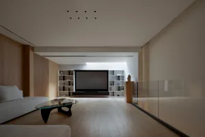 A modern living room featuring a minimalist design with wood flooring, a glass coffee table, and a large screen TV.