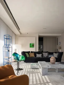 Modern living room with a black sofa, green and brown pillows, and a blue wire shelving unit.