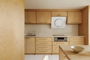 Modern minimalist kitchen with wood cabinets and countertops, featuring a white backsplash and a sleek, contemporary design.
