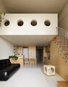 A modern open-plan living, dining, and kitchen area with wooden walls and floors, metal railings, and a black leather sofa.