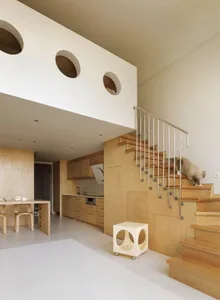 A modern home interior featuring wooden stairs and kitchen with a cat climbing the stairs.