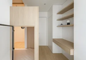 A minimalist interior featuring a white wall with wooden shelves and a door.