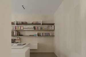 A well-organized and modern home office with floating shelves filled with books and a desk with a notebook and pen.