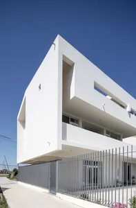 A modern building with a white concrete exterior, featuring a minimalistic design with large windows and a flat roof.