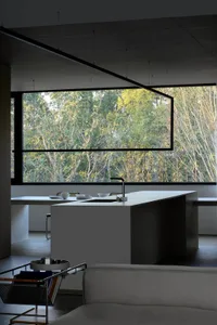 Modern kitchen interior with concrete island and large windows overlooking greenery.