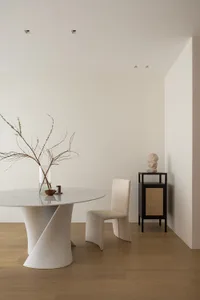 A modern dining room with a white marble table, a fabric chair, and a black side table with a sculpture.
