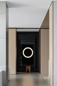 Modern minimalist entrance featuring a black glass wall, circular light fixture, and wood bench.