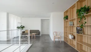 A modern minimalist living room with a grey couch, wooden chair, and bookshelf.