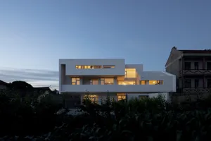 A modern residential building with concrete exterior, illuminated windows, and a minimalist design.