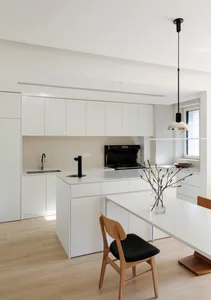 A minimalist kitchen with white cabinets, a hanging glass pendant light, and a light wood floor.