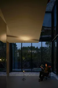 A modern interior design featuring a glass window with a person reading a book at dusk.