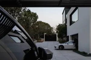A modern garage with a white sports car parked inside. The exterior features large windows and doors, and the surrounding are