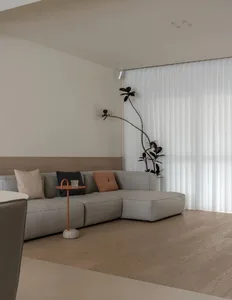 A minimalistic living room with neutral-colored furniture and a large window with vertical blinds.
