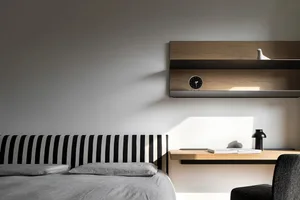 Modern minimalist bedroom featuring a bed with a black and white striped headboard and a light wood desk with a clock on it.