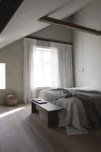 A minimalist bedroom with grey bedding, wooden flooring, and exposed beams.