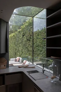 Modern kitchen featuring a large glass window overlooking lush greenery, with a sleek countertop and contemporary cabinetry.